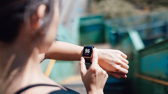 Uma mulher usa um aplicativo de fitness em seu telefone, sincronizado com um dispositivo de monitoramento vestível em seu pulso.